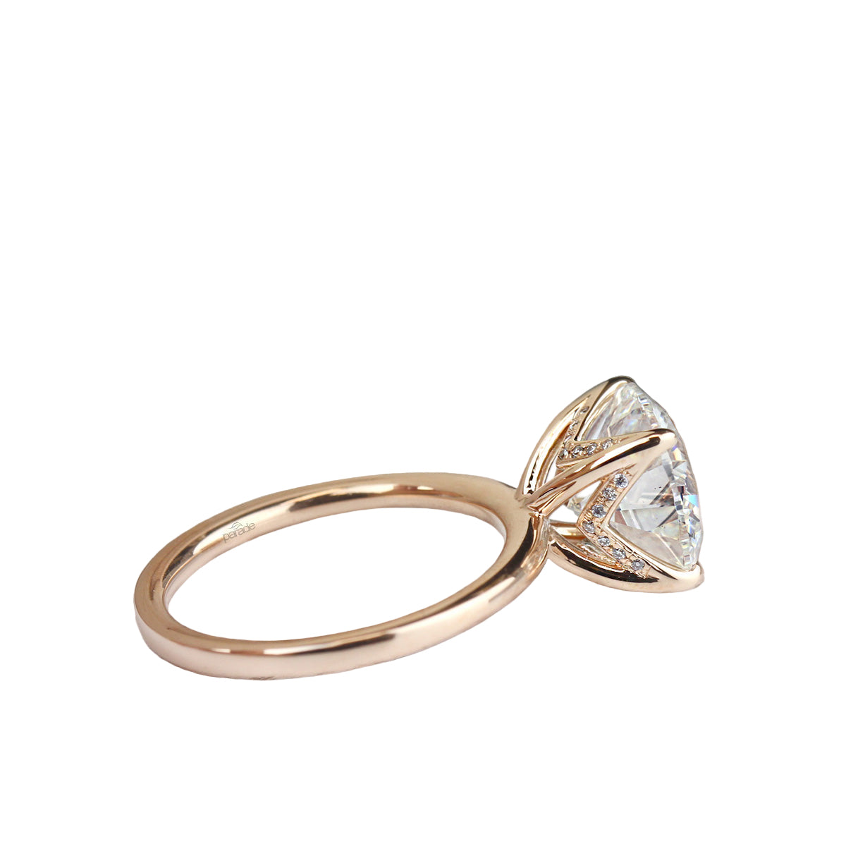A white gold solitaire ring mounting with a diamond chevron basket, displayed on a wooden surface with pine cones in the background.