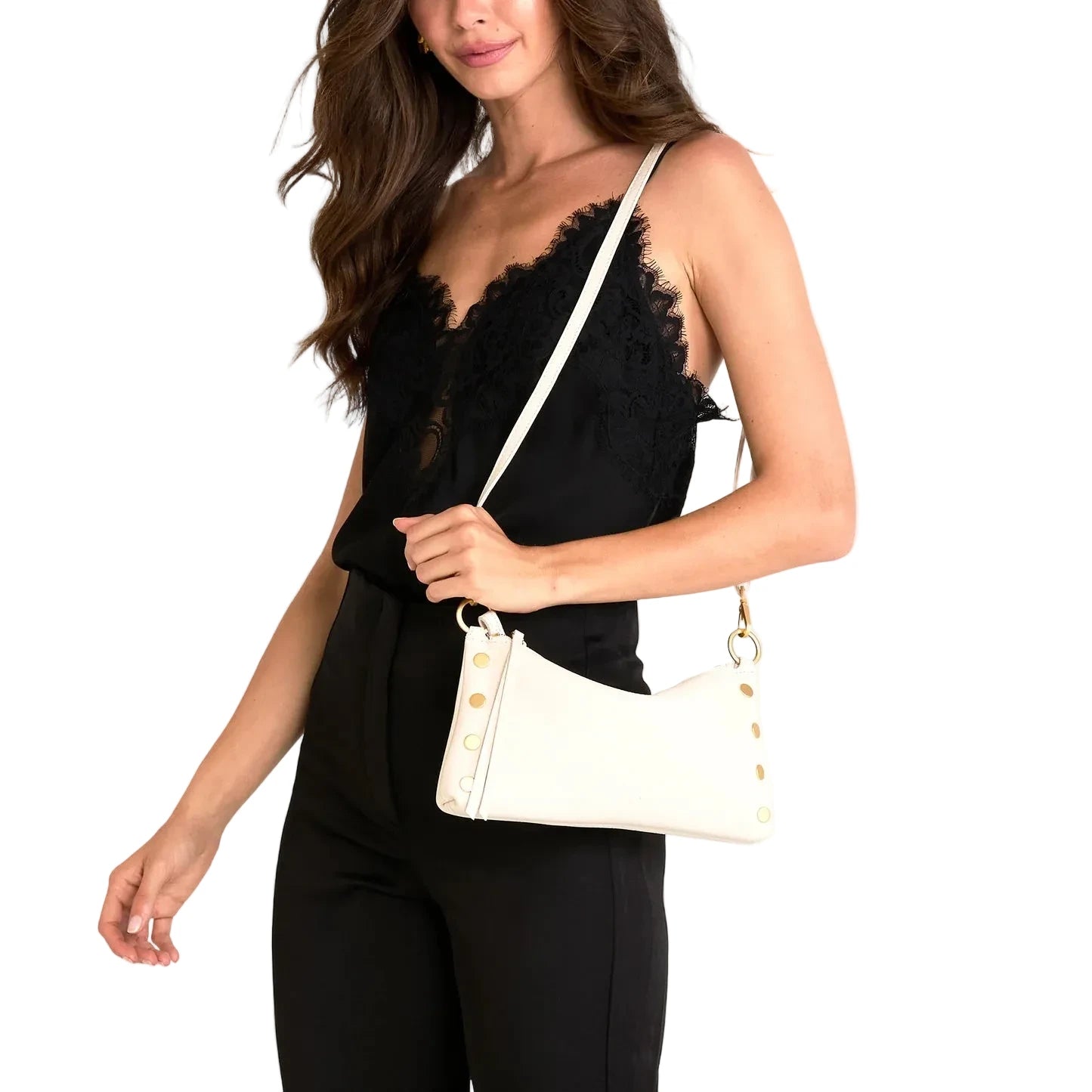 Woman wearing a black lace top and black pants, holding a cream handbag.
