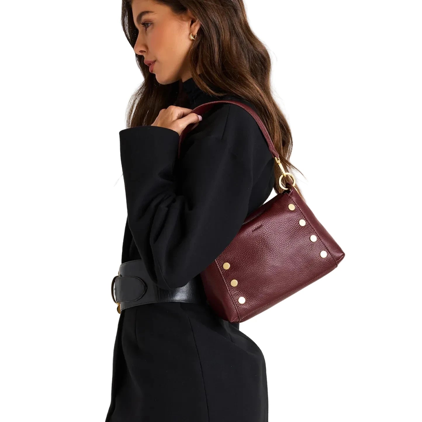 Woman holding a maroon handbag with gold studs against a beige background