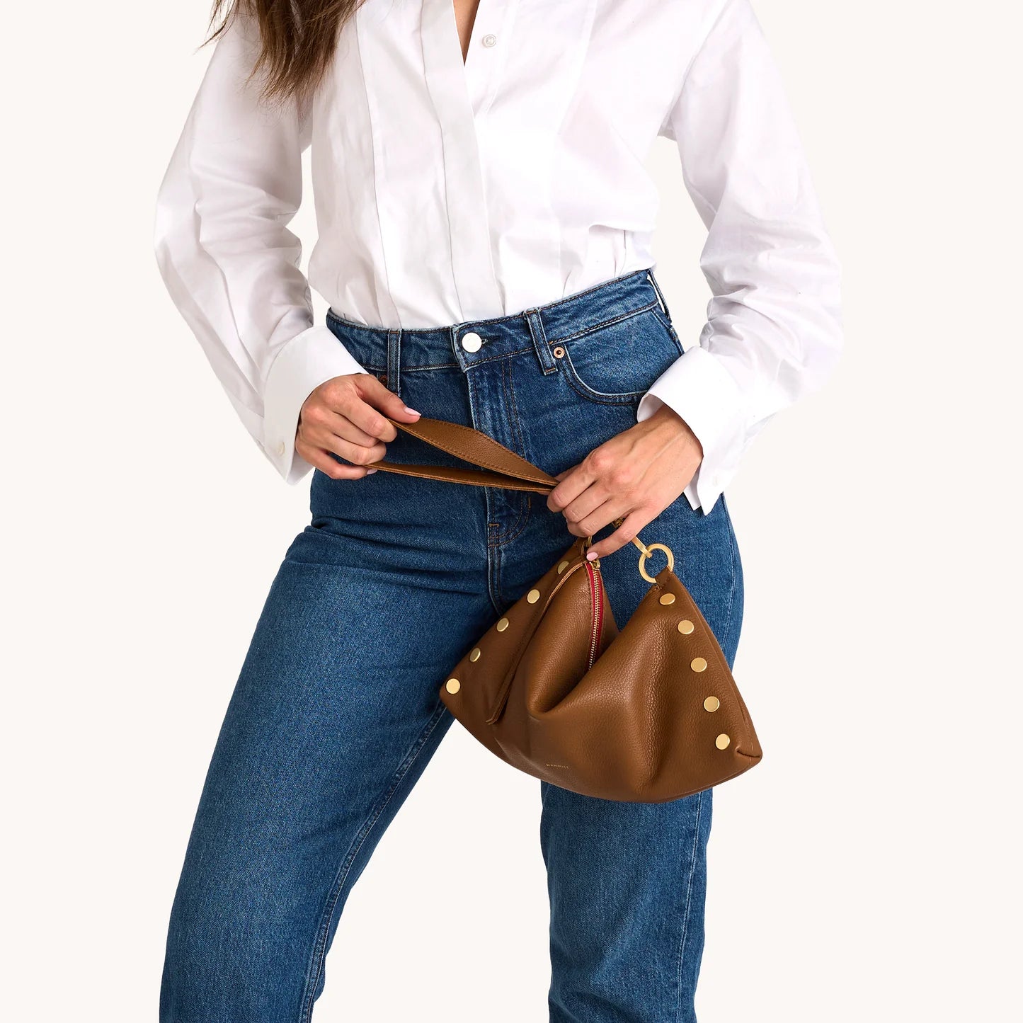 Person holding a brown leather handbag with gold studs on a white background