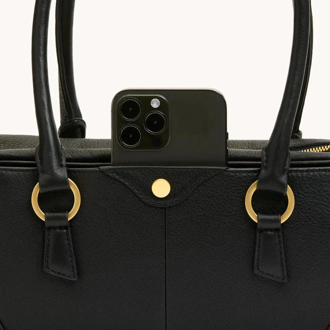 Black leather handbag with gold accents and a smartphone inside