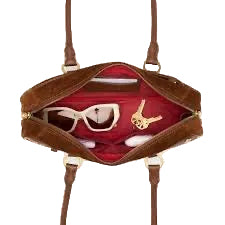 Brown handbag with a red interior containing jewelry on a white background