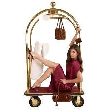 Woman sitting on a gold luggage cart with a white garment and brown bag against a beige background
