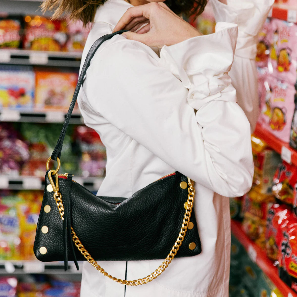 Person holding a black handbag with gold chain in a store setting