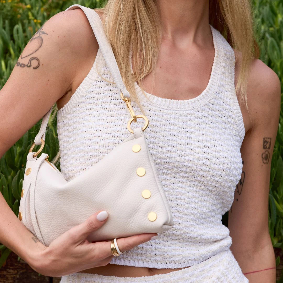 Woman holding a white handbag with gold accents in a nature setting