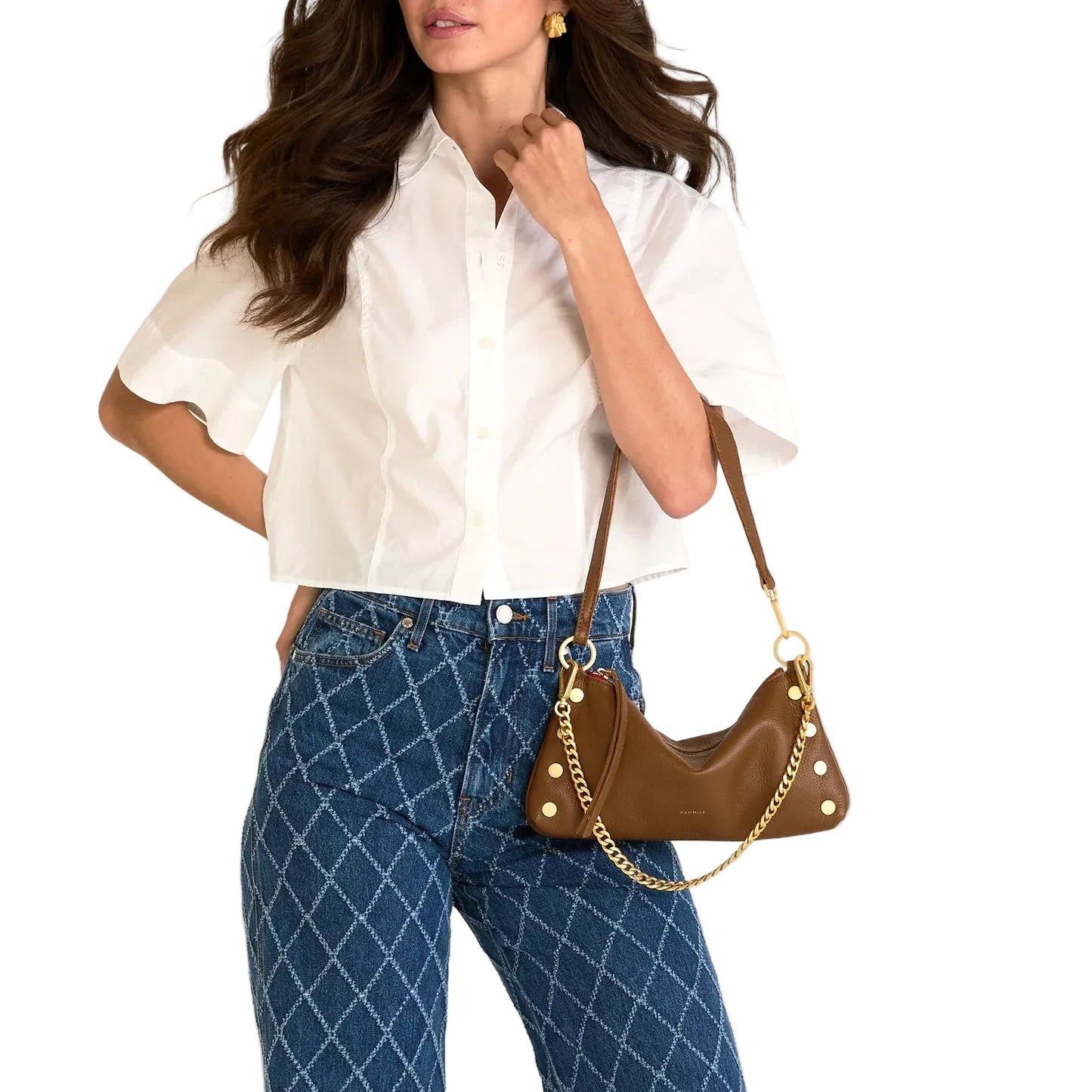 Woman wearing a white blouse and blue jeans, holding a brown handbag with gold accents.