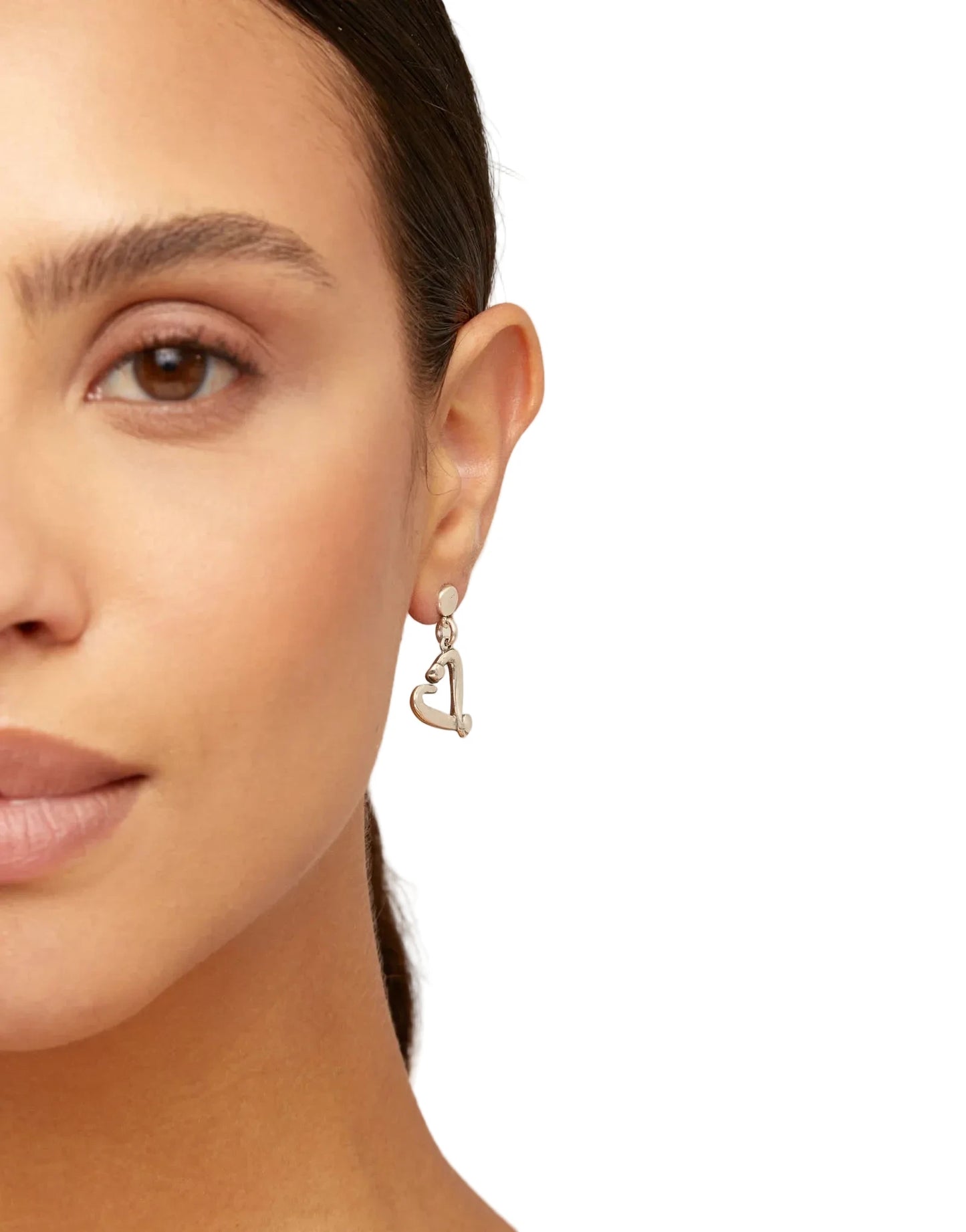 Close-up of a woman wearing a heart-shaped earring on a beige background