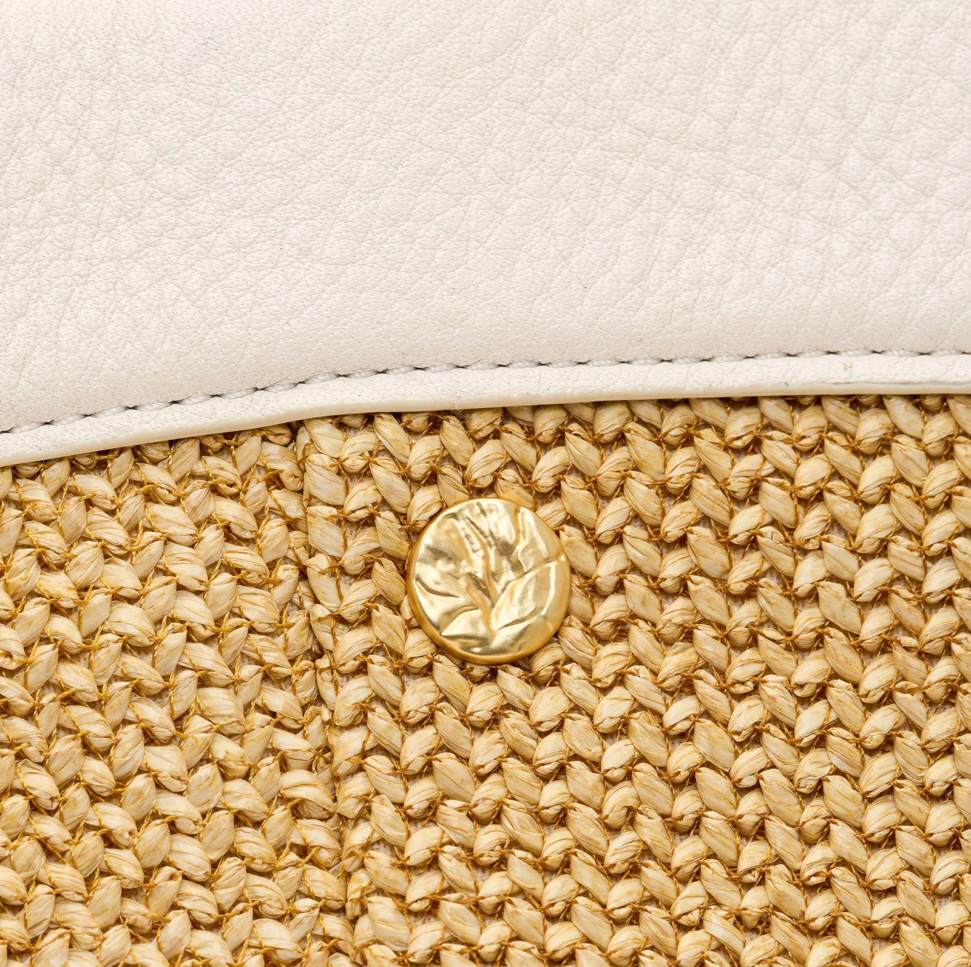 Close-up of a white leather clutch with a gold button on a beige woven texture.