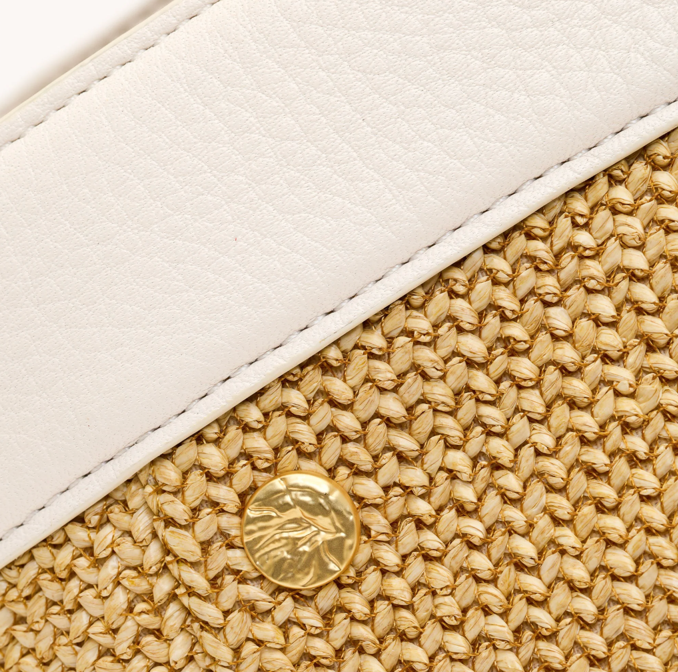 Close-up of a white and beige handbag with a gold button detail.