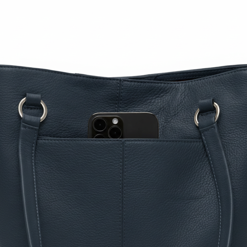 Navy blue leather handbag with a phone in the pocket on a white background