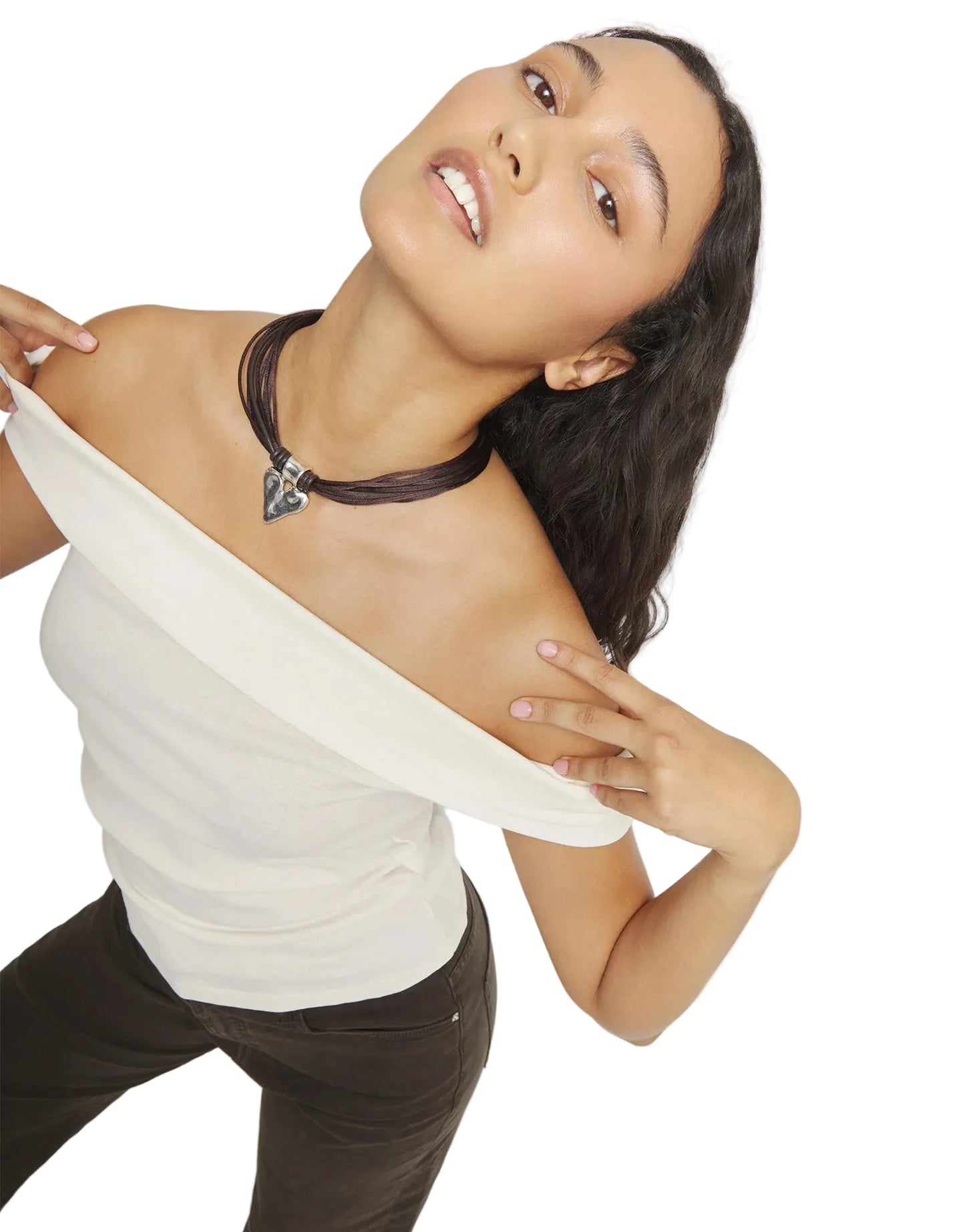 Woman wearing a white top and brown pants with a necklace on a plain background