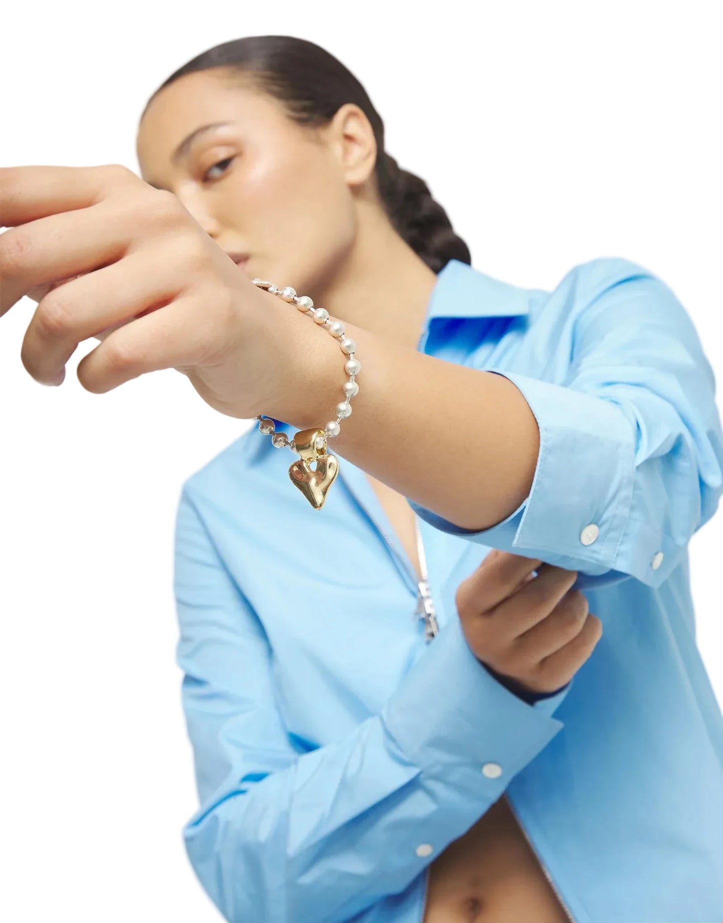 Person wearing a blue shirt with a pearl bracelet on a plain background