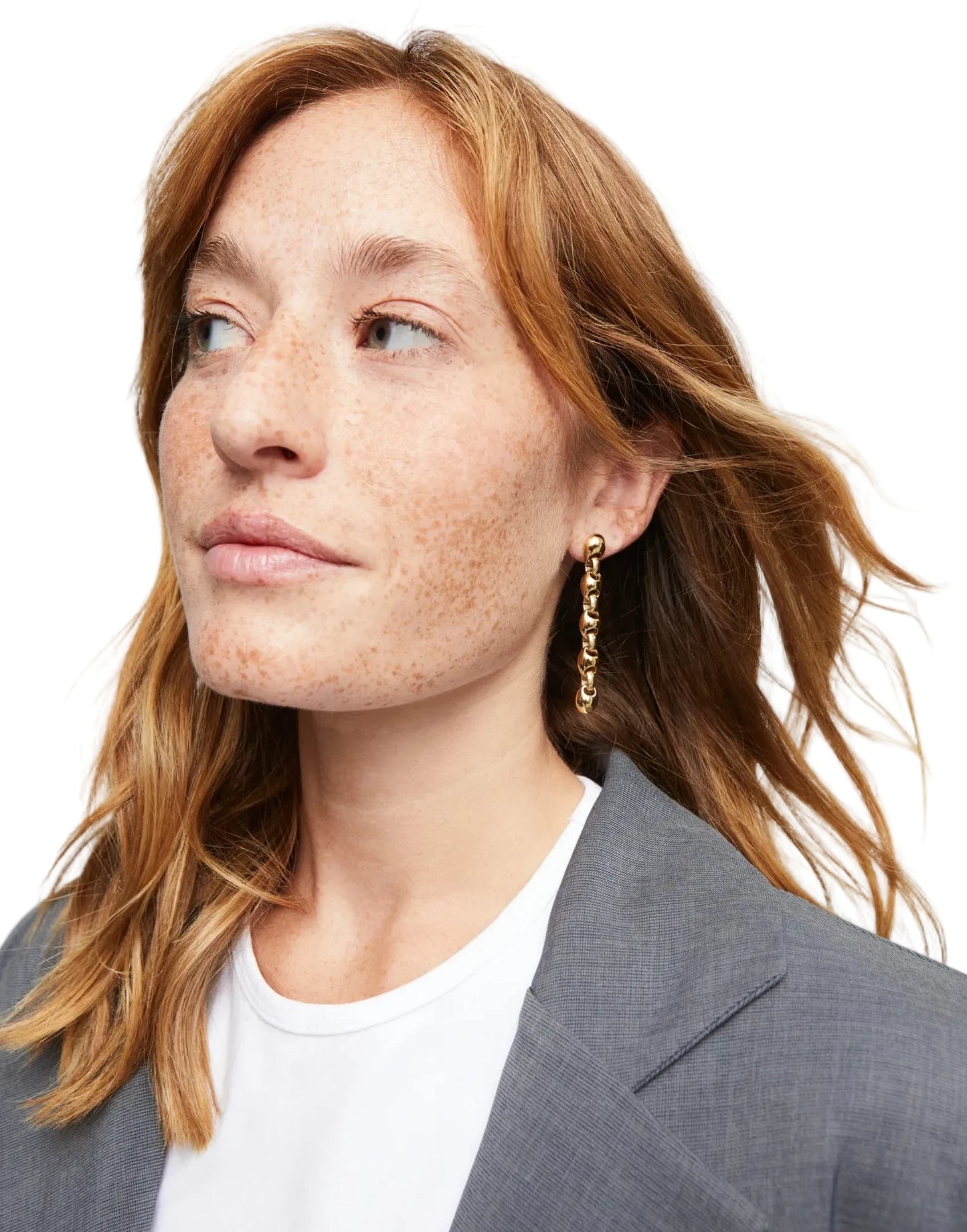 Woman with freckles wearing a gray blazer and white shirt against a light background