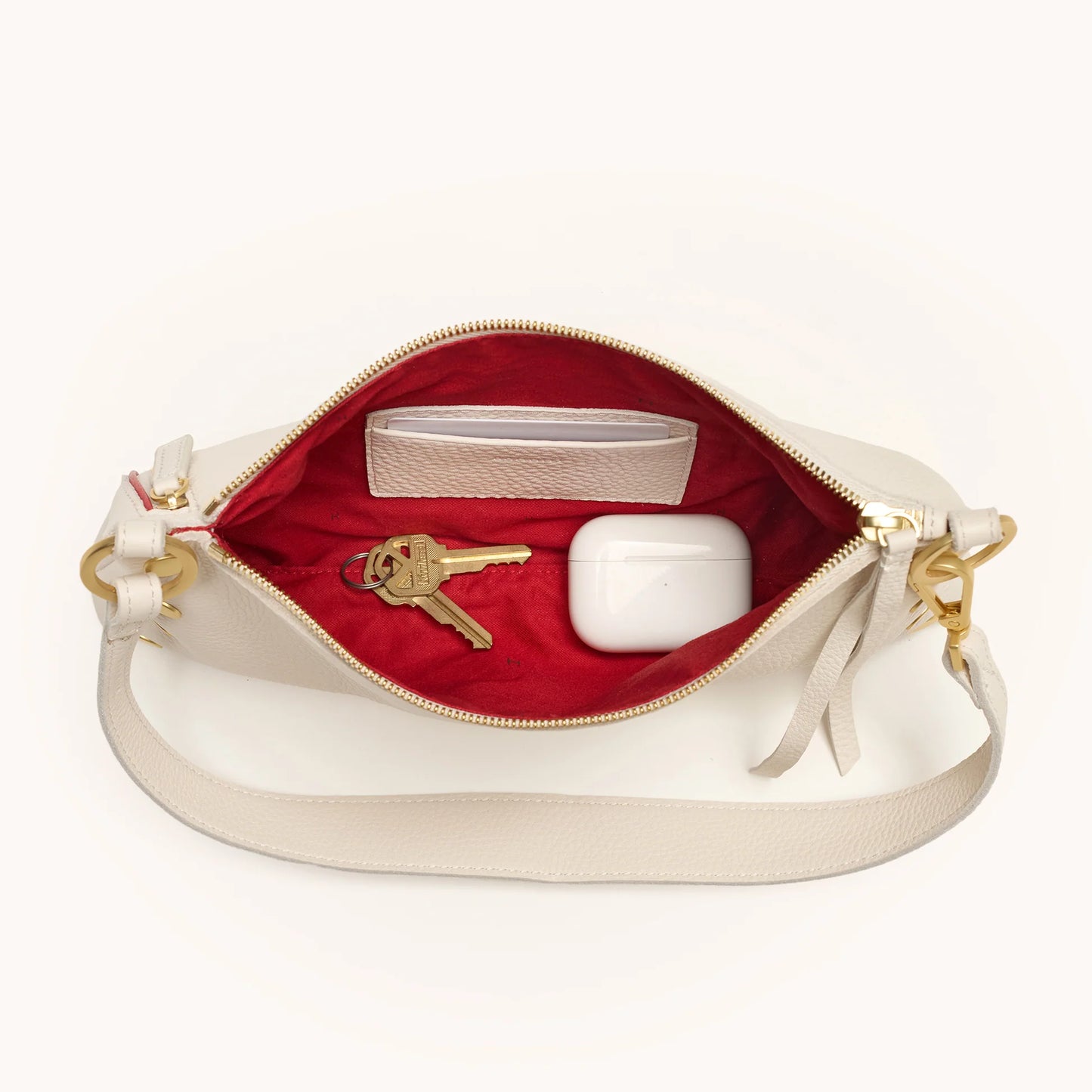 Open cream handbag with red interior showing gold keys, and a small white box.