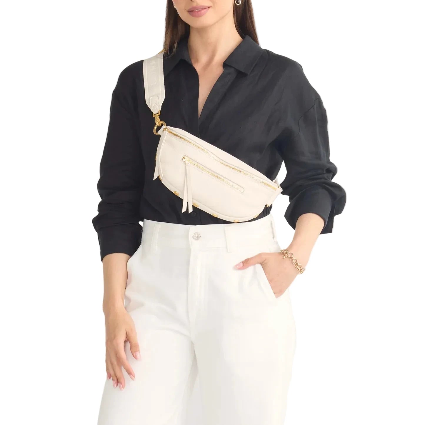 Woman wearing a black shirt and white pants with a cream crossbody bag on a white background
