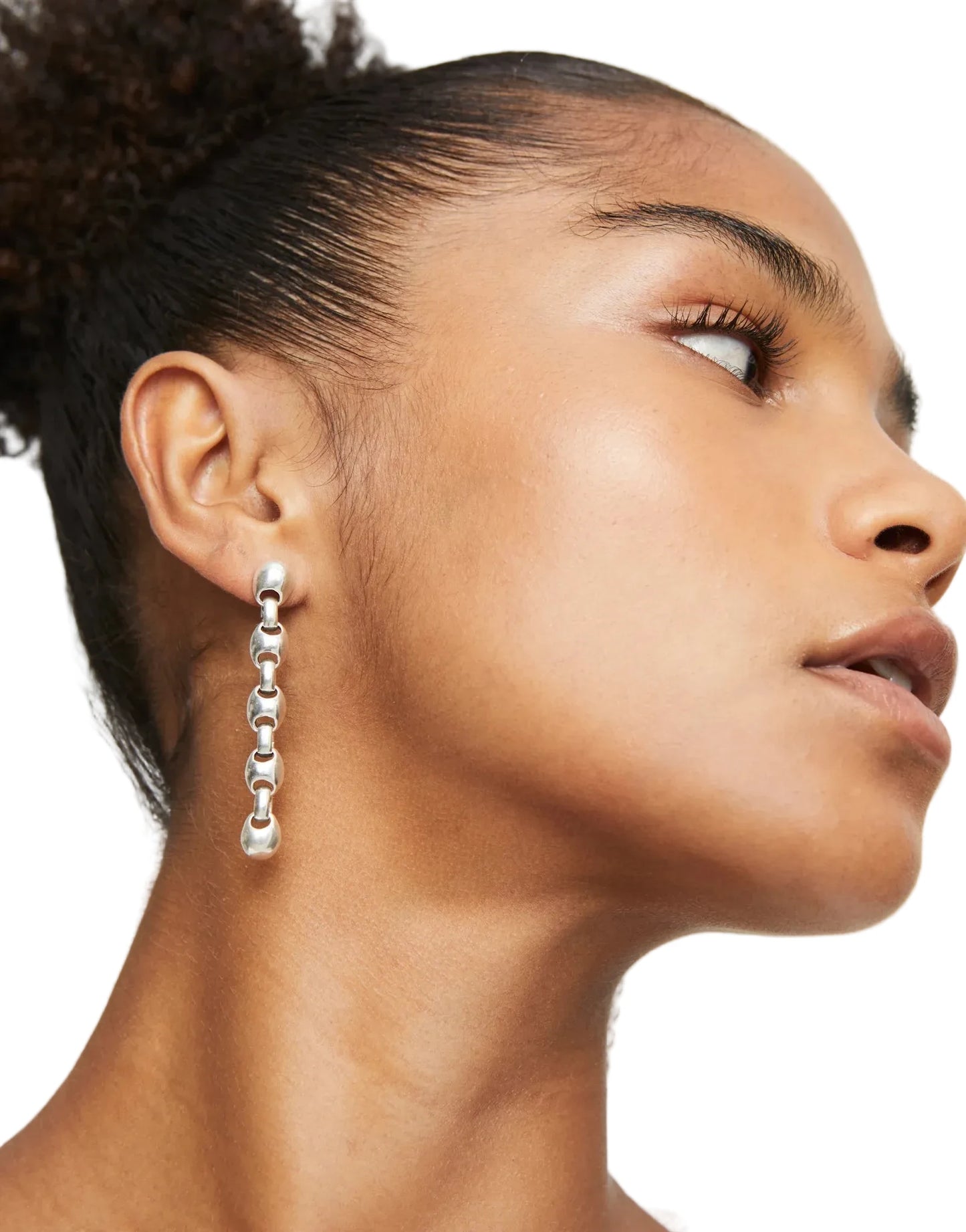 Close-up of a woman wearing a silver chain earring against a neutral background
